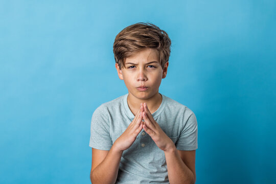 A pre-teen tween boy being silly with his hands in a praying or guru thinking mode on a colorful blue background with copy space