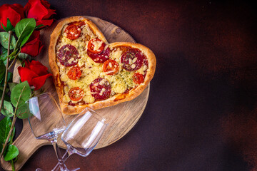 Heart shaped pizza with tomatoes and mozzarella and pepperoni on dark table background. Idea for Valentine day dinner, dating, lunch or dinner February 14 menu for couples, top view copy space