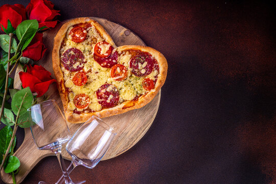 Heart shaped pizza with tomatoes and mozzarella and pepperoni on dark table background. Idea for Valentine day dinner, dating, lunch or dinner February 14 menu for couples, top view copy space