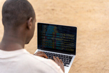 From above African American man in casual clothes using laptop to create code for software while working remotely on beach