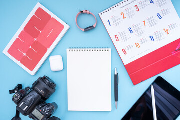 Vacation, trip or holiday planning concept - Public Holiday calendar with notepad, pen, earphone, sport watch, camera and tablet on blue background. Top view flat lay copy space.