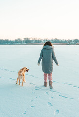 Winter walk of young beautiful brunette woman wearing warm clothes in snow with dog golden. Snowing winter concept.