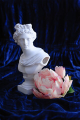 apollo sculpture next to a pink flower on a blue velvet background