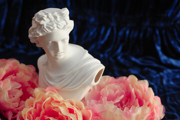 Greek sculpture among pink peonies on a blue velvet background. close up. copy space
