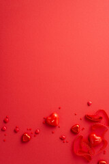 Valentine's Day concept. Top view vertical photo of heart shaped candies ribbon candles and sprinkles on isolated red background with empty space