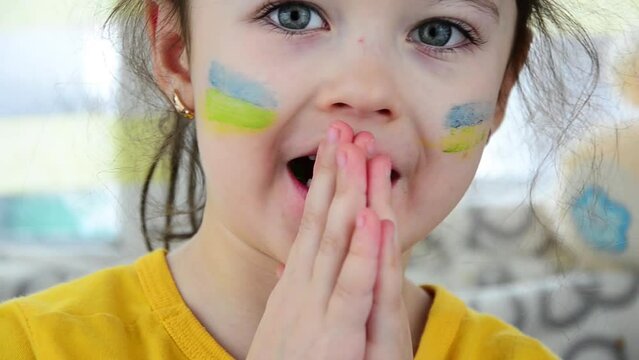 Ukrainian child prays for peace. War in Ukraine. Girl with Ukrainian symbols. The shelling of Ukrainian cities. Destruction during the war in Ukraine. Peace concept. Children against war. 