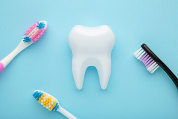 White healthy tooth model and toothbrushes on blue background. Dental care and healthcare concept.