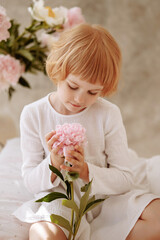 Girl 6-7 years old in a white dress sits on a vintage bed