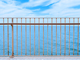 View on a clear blue sea under the cloudy sky through a fencing of a breakwater