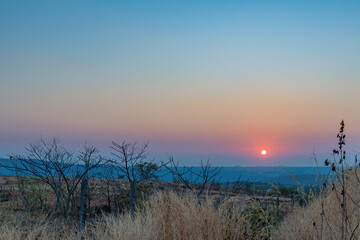 A sunset over a mountain. The sun's rays shining on the peaks create a range of colors, from warm oranges and yellows to cool purples and blues. 