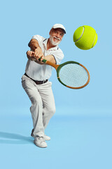 Fototapeta na wymiar Returning ball. Portrait of handsome senior man in stylish white outfit playing tennis over blue background. Concept of leisure activity, hobby, lifestyle