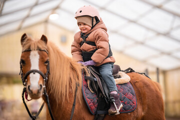 Little Child Riding Lesson. Three-year-old girl rides a pony and does exercises
