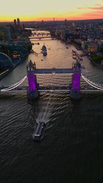 Aerial vertical shot of Tower Bridge Purple Illuminated, London City Skyline The Shard And Thames River Boat Passing, London Skyscraper UK, United Kingdom At Sunset