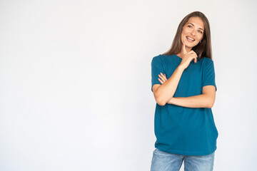 Fototapeta premium Portrait of pensive young woman holding her chin with finger. Female Caucasian model with brown hair and grey eyes in turquoise T-shirt and casual jeans smiling propping her head. Advertising concept