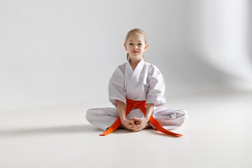A little girl in a white kimono sits on a light background, karate.