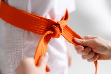 The coach's caring hands are tying the belt on the children's kimono.