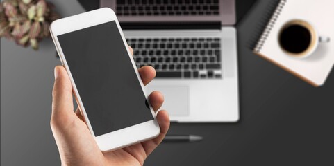 Hand holding a modern smartphone on office desk background.