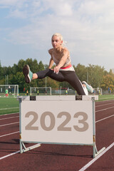Young woman athlete runnner running hurdles and jumps over 2023 year at the stadium outdoors