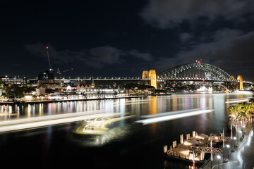 Fototapeta na wymiar Light trails at night of ferries arriving and departing from Circular Quay in Sydney with Sydney Harbour Bridge in the background