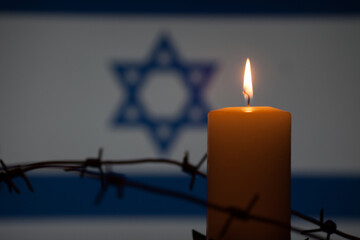 Burning candle with barbed wire on Israel flag background. International Holocaust Remembrance Day,...