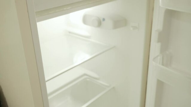 The hand of a man opening a vintage fridge, discovering that it's completely empty, showing disappointment. Angled closeup shot.
