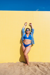 Beautiful and confident plus size woman having fun at the beach, posing on colorful wall background...