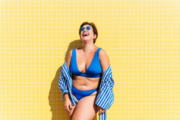 Beautiful and confident plus size woman having fun at the beach, posing on colorful wall background - concepts about body acceptance, body positive, self confidence and body care - Powered by Adobe