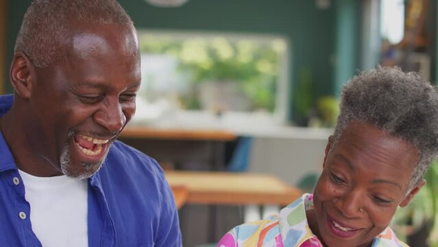 Smiling senior couple reliving memories sitting on sofa at home and looking through photo album together - shot in slow motion