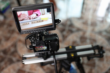 Digital camera with external monitor on camera slider filming woman typing on keyboard.