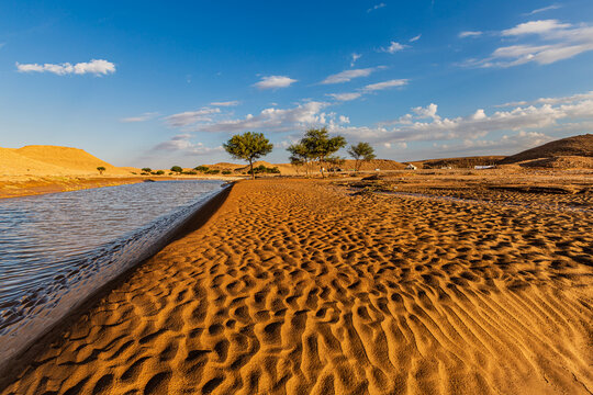 Desert landscape and lake after rain with tents in distance, Saudi Arabia