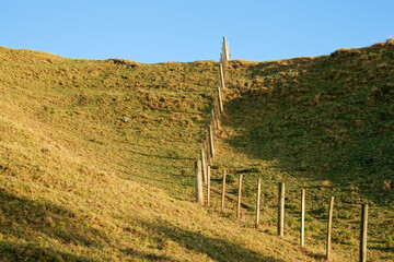 Fototapeta na wymiar Fence leading up and over slope under blue sky
