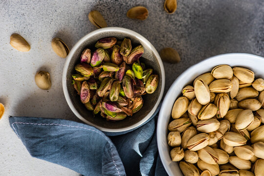 Overhead view of a bowl of pistachio nuts in shells next to a bowl of shelled pistachios