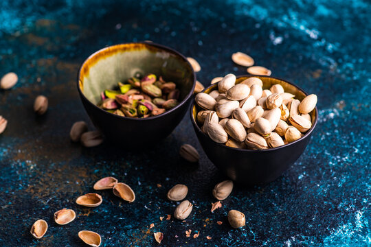 A bowl of pistachio nuts in shells next to a bowl of shelled pistachios