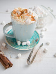 Coffee in a blue cup with cinnamon, cream and marshmallows on a white wooden background.