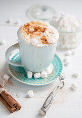 Coffee in a blue cup with cinnamon, cream and marshmallows on a white wooden background.