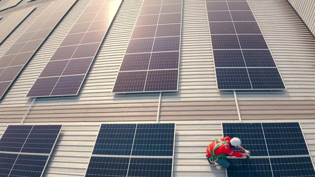 Male engineer maintaining solar cell panels on building rooftop. Technician working outdoor on ecological solar farm construction. Production of renewable energy concept.