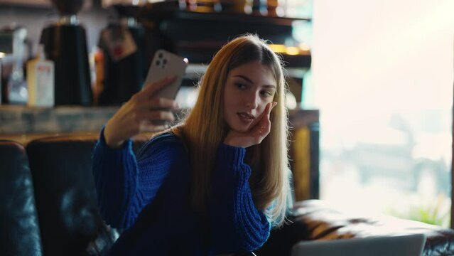 Attractive woman looking at her cell phone and taking a selfie in a modern cafe