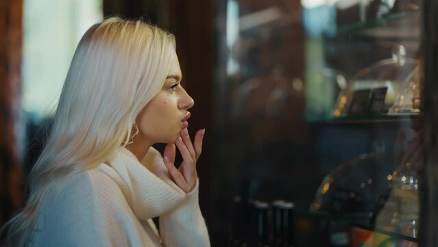Close up of a blonde woman looks at cakes at showcase and makes a choice