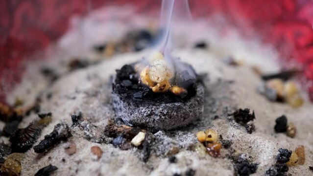 Mixture of aromatic incense resin, frankincense (olibanum), styrax and rose blossom petals burning on hot charcoal in a red incense bowl - closeup