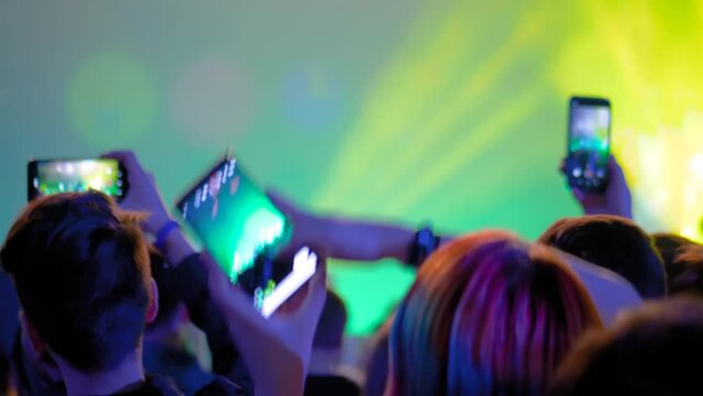 Slow motion: teenagers hands taking photo or recording video of live music concert with smartphone. Crowd partying in front of stage. Photography, entertainment, technology concept