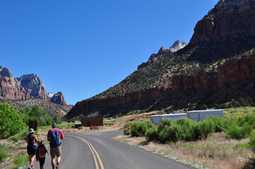People walking along road beside huge red rock mountains