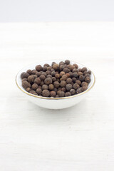 Allspice peas scattered in a white bowl on white wooden background