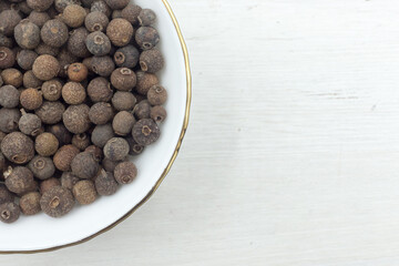 Allspice peas scattered in a white bowl on white wooden background