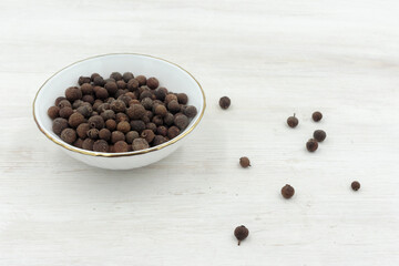 Fototapeta na wymiar Allspice peas scattered in a white bowl on white wooden background