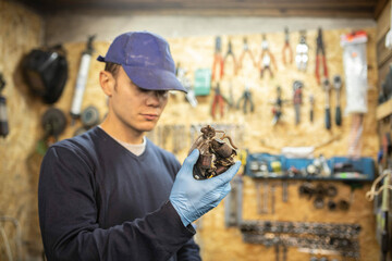 male mechanic holds in his hand an electric coil of a car generator in a workshop.