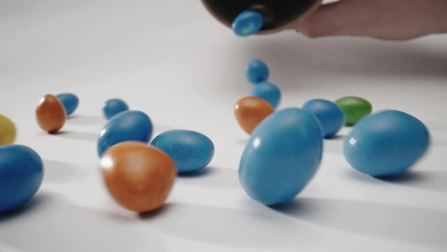 Sweet candies falling, scattering in different directions and rolling on white surface. Slow motion