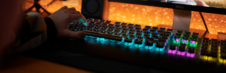 Hands of gamer man playing video games on computer in dark room using backlit colorful keyboard © stenkovlad