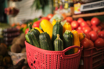 red basket with green and yellow zucchini in the middle of farmers' market for sale with selective focus