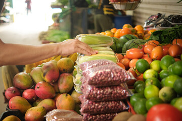 man's hand picking tropical fruits and vegetables at farmer's market stall