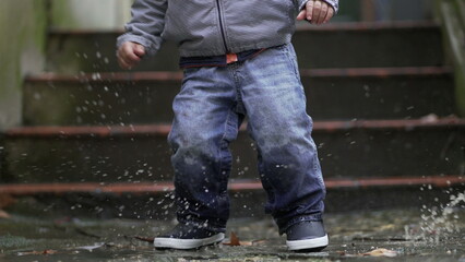 Toddler boy splashes into puddle of water. Child plays with puddles